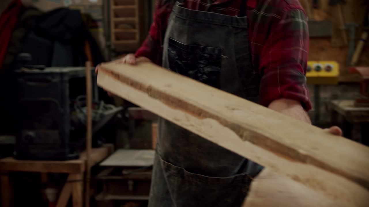 рабочий в деревообрабатывающей мастерской, берет доску и ставит ее на машину в деревообработывающей мастерской небольшого производителя мебели.