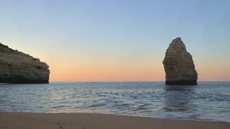 ground level footage of gentle waves lapping on a beautiful deserted beach in algarve, portugal at sunrise showing sandstone cliffs and a sea stack