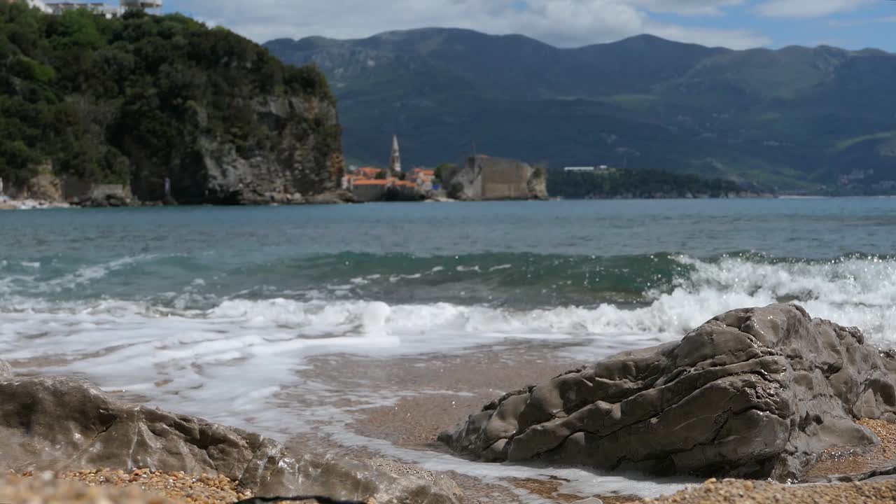 Onde che si infrangono dolcemente sulla spiaggia, con la Città Vecchia di Budva sullo sfondo, Montenegro.