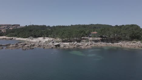 Raw-Aerial-Footage-of-Rocky-Shore-with-Woods-and-Buildings-Around