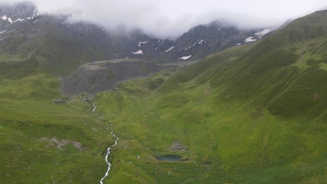 drone shot of lake and river in the middle of mountains with cloud and fog in the background caucasian mountains