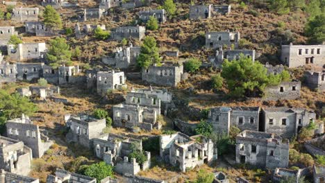 aerial drone panning up showing the abandoned buildings and homes left in ruins on the mountain of kayakoy village on a sunny summer day in fethiye turkey