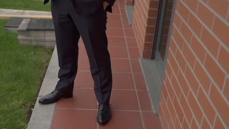lower body shot of a man in a dark suit and black dress shoes standing near a brick wall