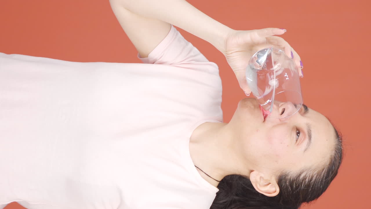 그 여자가 물을 마시는 수직 비디오입니다.