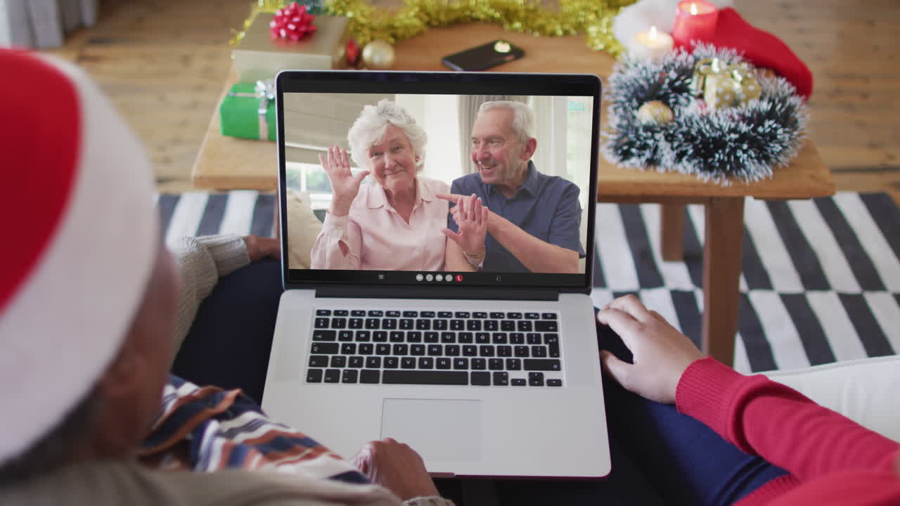 madre y hija afroamericanas usando una computadora portátil para una videollamada de navidad con la pareja en la pantalla