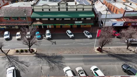 overhead shot of vehicles moving along a quiet urban street lined with shops and parked cars in a residential area under clear daylight