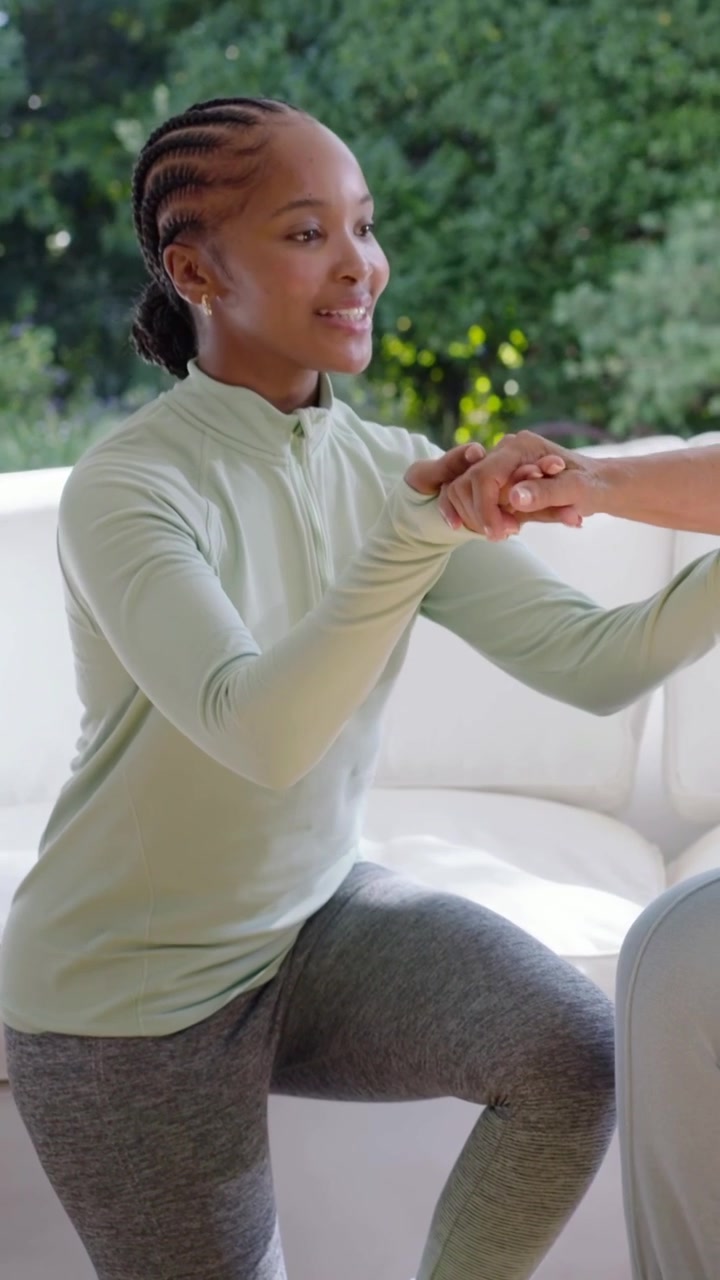 Vertical video: Guiding green aid putting hand on blue senior, guiding arm on pink ball for balance