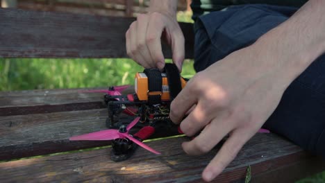 pilot strapping battery of an fpv drone on wooden bench outdoor