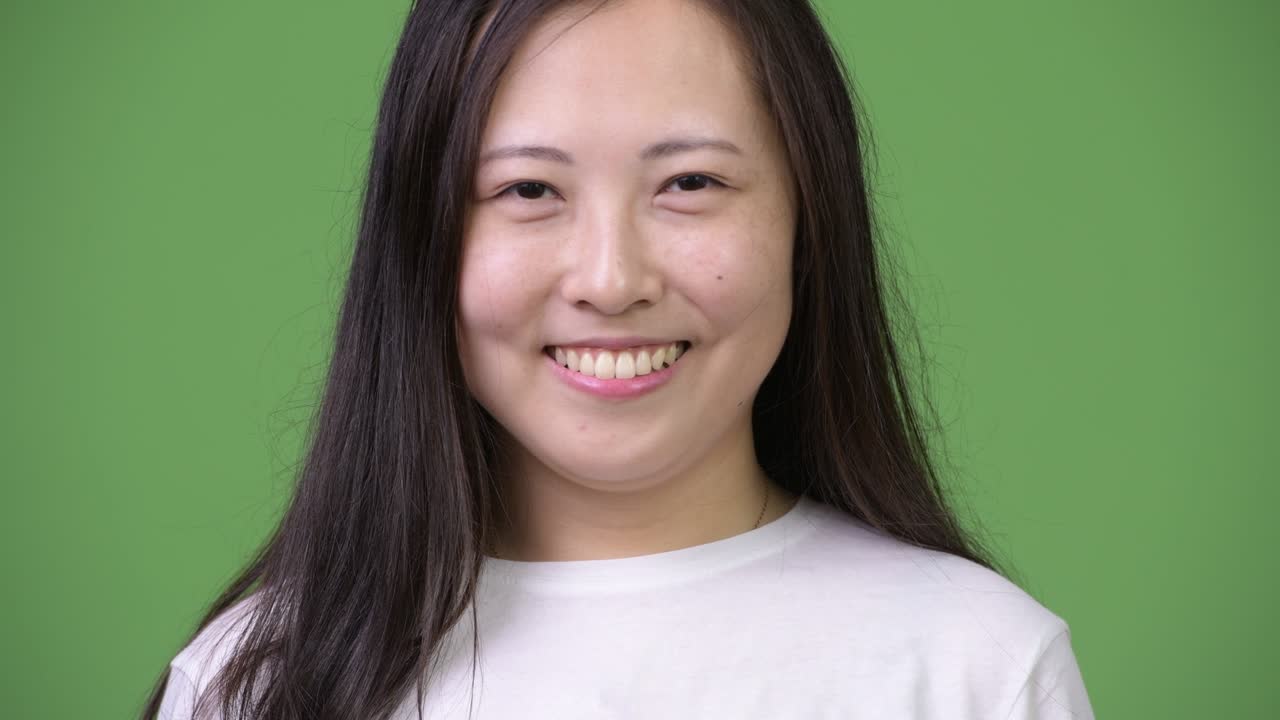Young happy Asian woman smiling against green background