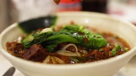 chopsticks lifting meat from noodle bowl