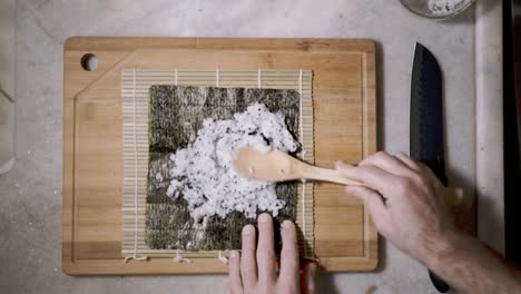 top down time lapse of two hands spreading rice with chai seeds on a mat and seaweed nori sheet to make sushi