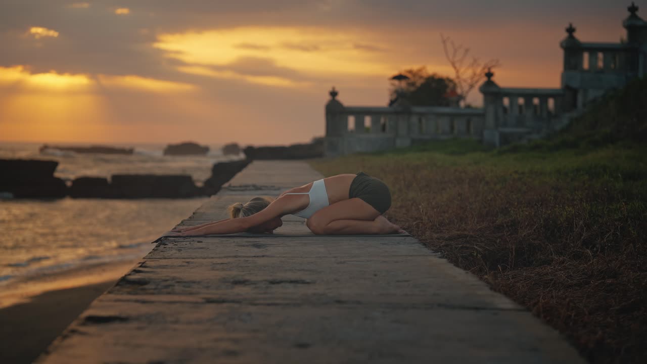 Fit woman practicing child pose with moody sunset in background, yoga routine