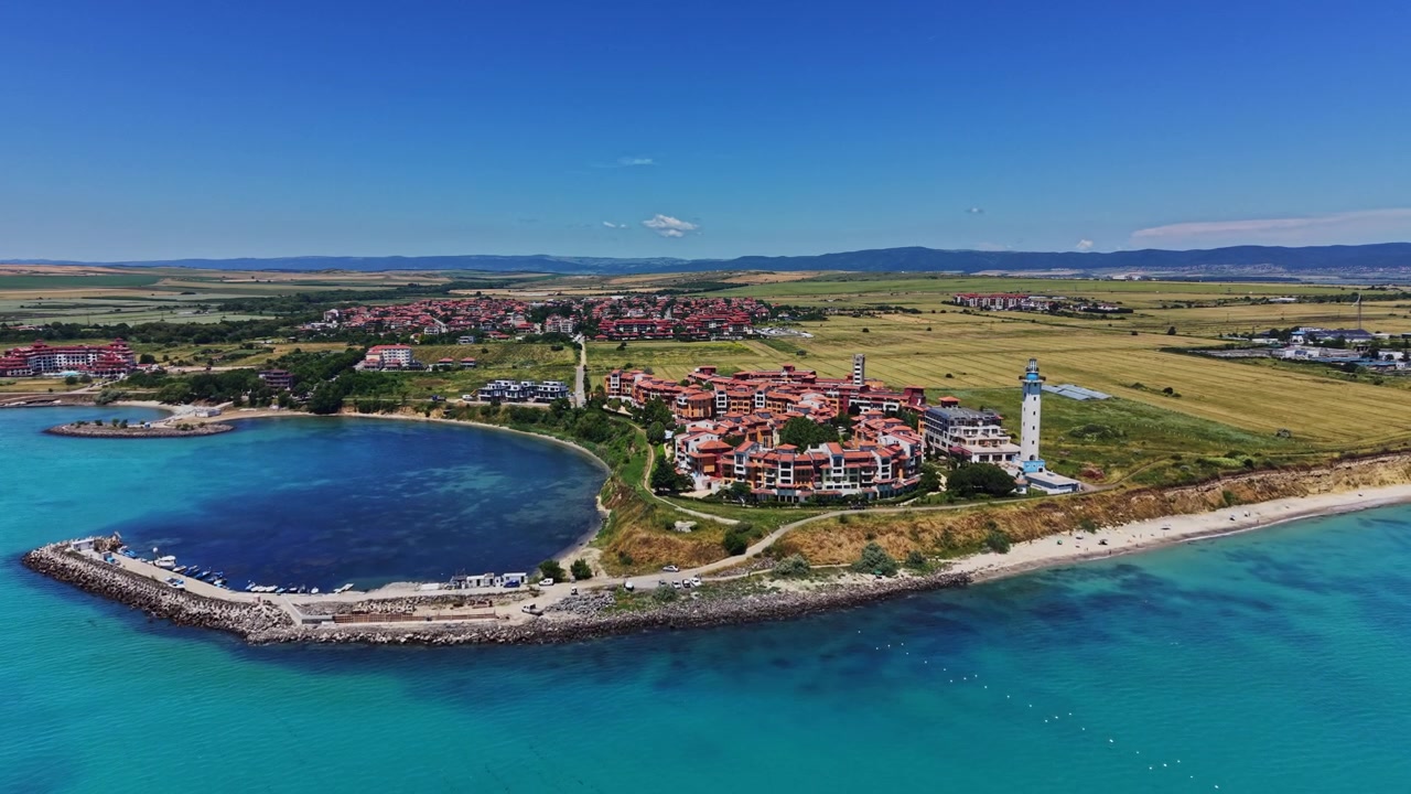 Güneşli bir günde berrak su ve uzaktaki binalarla kıyı manzarası