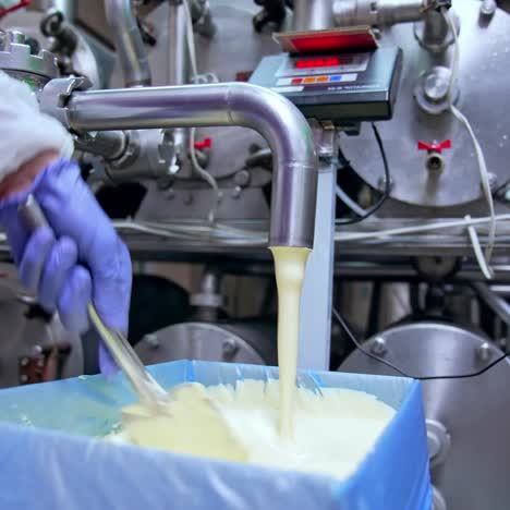 liquid butter pouring into a large box. use of spatula to flatten the dairy product in the container. factory worker holding his hand at the faucet to stop the flow of butter
