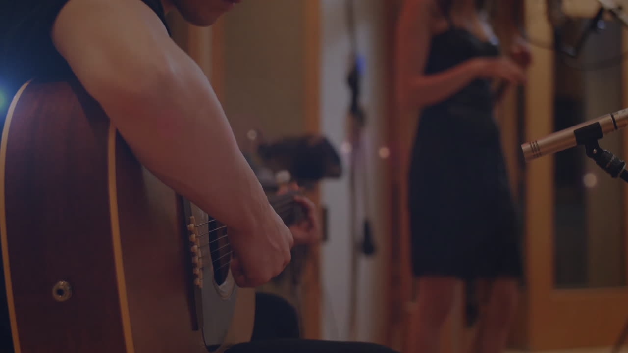 Musician playing acoustic guitar in music studio, vocalist syncing with floating microphone icons