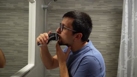 Married-man-in-glasses-shaving-beard-in-bathroom,-checking-progress