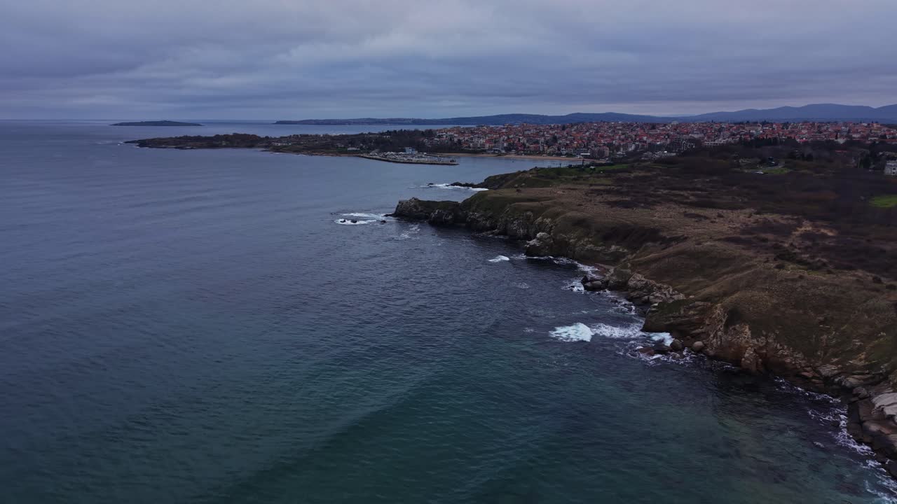 Vista della costa con onde e scogliere vicino a una città al tramonto