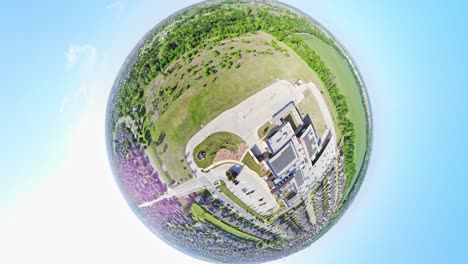 rising above a windmill and then pulling back to an asteroid, tiny planet view of the surrounding area which includes a neighborhood, school, greenspace, and a large corn filed in the distance