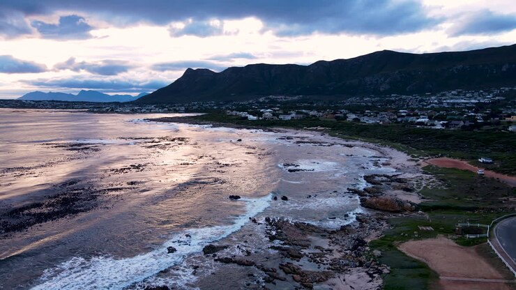 Vista drone al tramonto della costa di Sandbaai con onde che si infrangono e sfondo montuoso