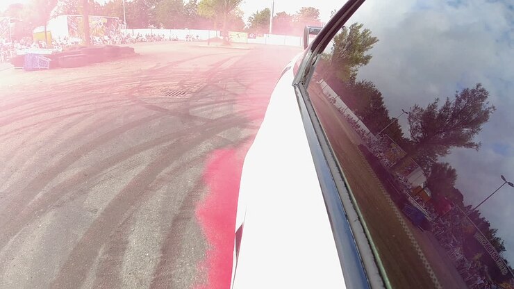 Primo piano di un finestrino auto oscurato mentre derapa sulla strada asfaltata con tracce di pneumatici ed emette fumo rosso. Spettacolo di acrobazie del Team Lagrin.