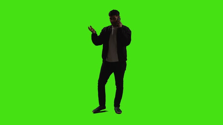 Giovane uomo che parla al telefono cellulare in piedi davanti a uno schermo verde con illuminazione a bassa chiave 1.