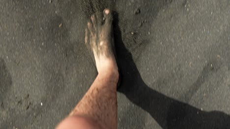 man walking barefoot on black sand beach, pov view