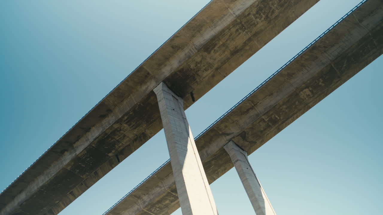 Low angle view of a large concrete bridge structure with clean geometric lines and symmetry against a clear blue sky. Minimal architectural composition with strong perspective