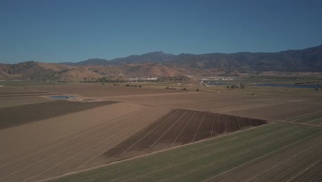 Aerial-view-of-empty-farmland-crop-fields-surrounded-by-California-mountains