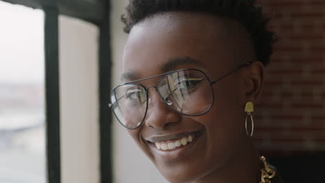 close up portrait stylish young african american woman student smiling happy enjoying successful lifestyle wearing trendy fashion glasses looking out window in modern apartment loft