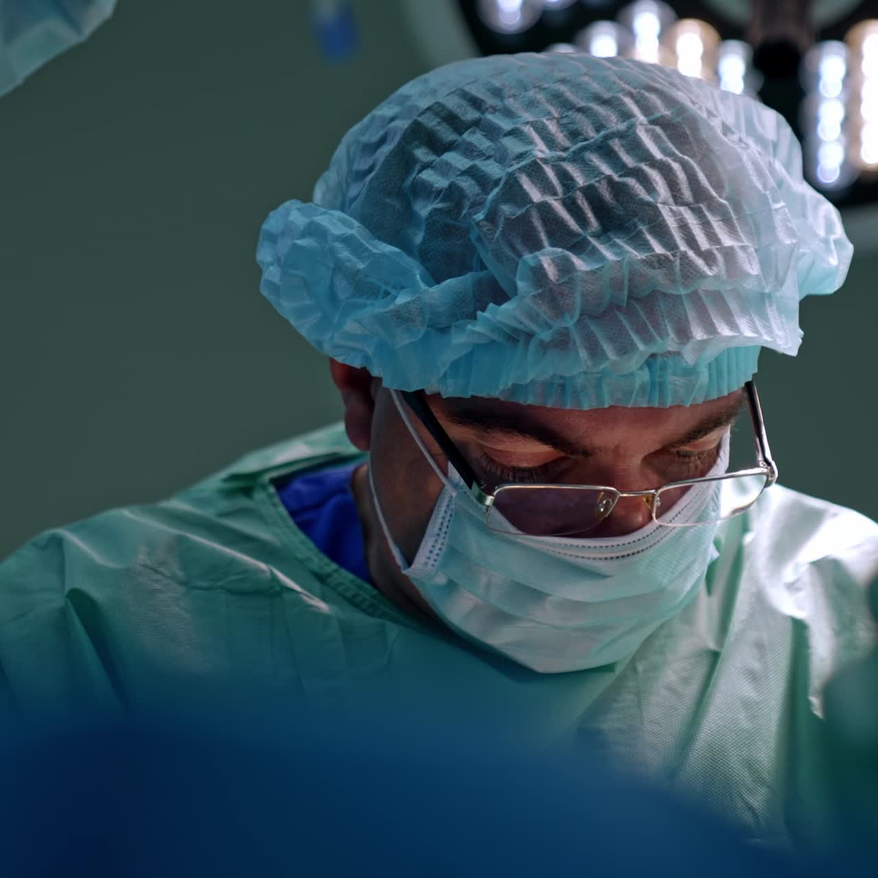 Male surgeon in glasses looking attentively at the operated area. Confident focused doctor at work. Close up portrait