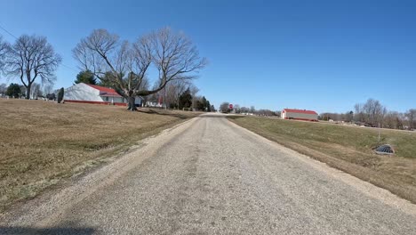 POV---Driving-on-country-road-past-cemetery,-barn,-and-empty-fields-in-early-spring-in-the-Midwest