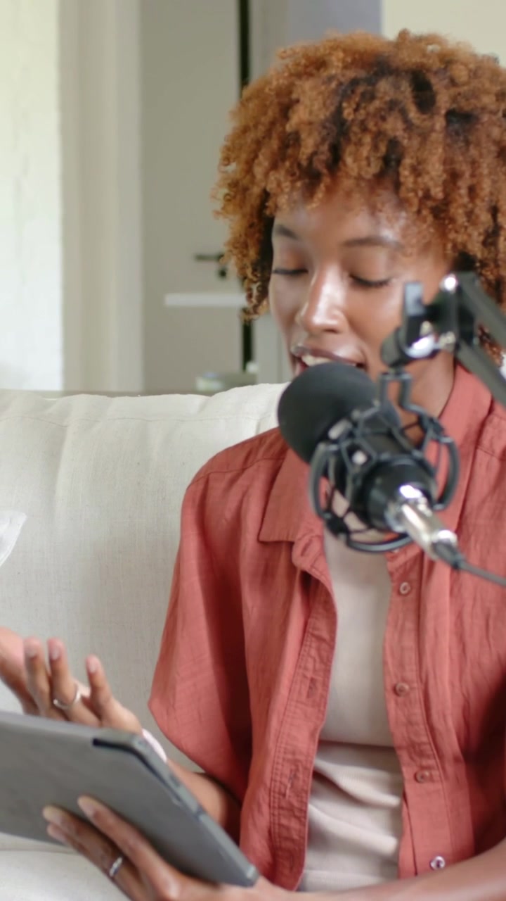 Vertical video: Recording, host in rust top, jeans reading tablet at home by boom mic, copy space