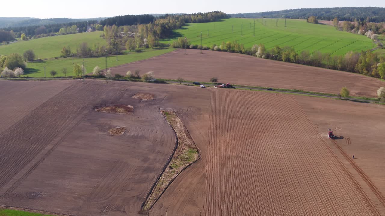 Drone zoom in over planted field towards working tractor with visible terrain lines and contrast