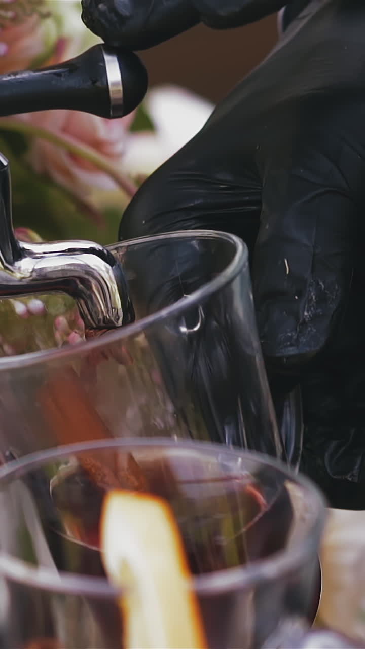 CU, slow motion: skilled bartender in black gloves fills glass cup with tasty red mulled wine from metal tag at wedding party extreme close view