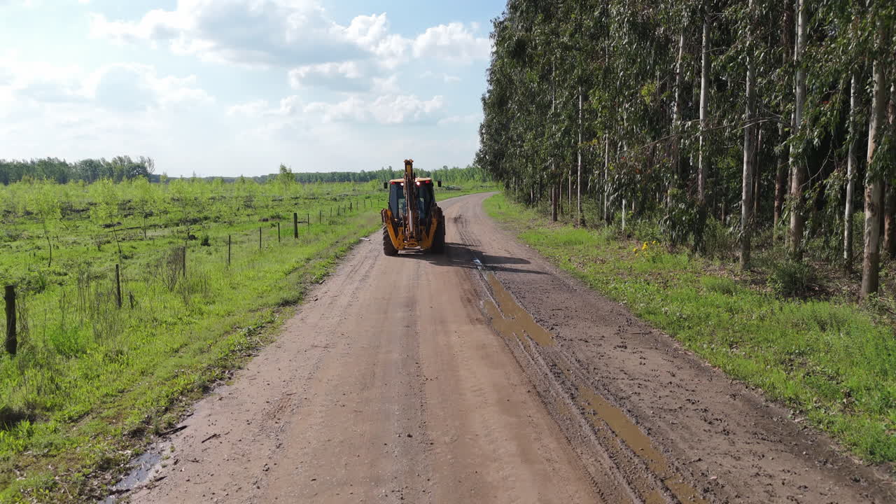 Tractor driving down a dirt road through agricultural fields, rural setting with open sky above, desending crane