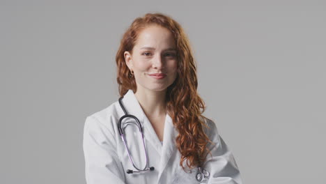 studio portrait of smiling female doctor with stethoscope in white coat against plain background