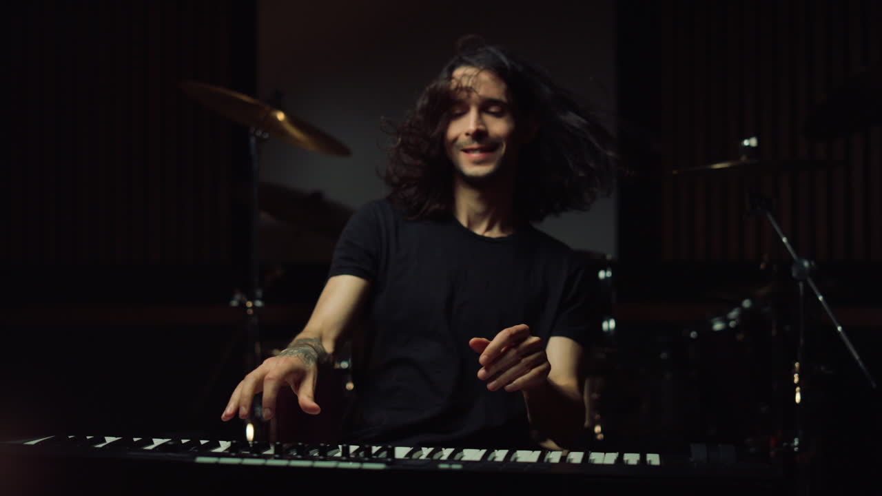 un hombre satisfecho tocando en una sala oscura, un tipo sonriente ensayando en un estudio de música.