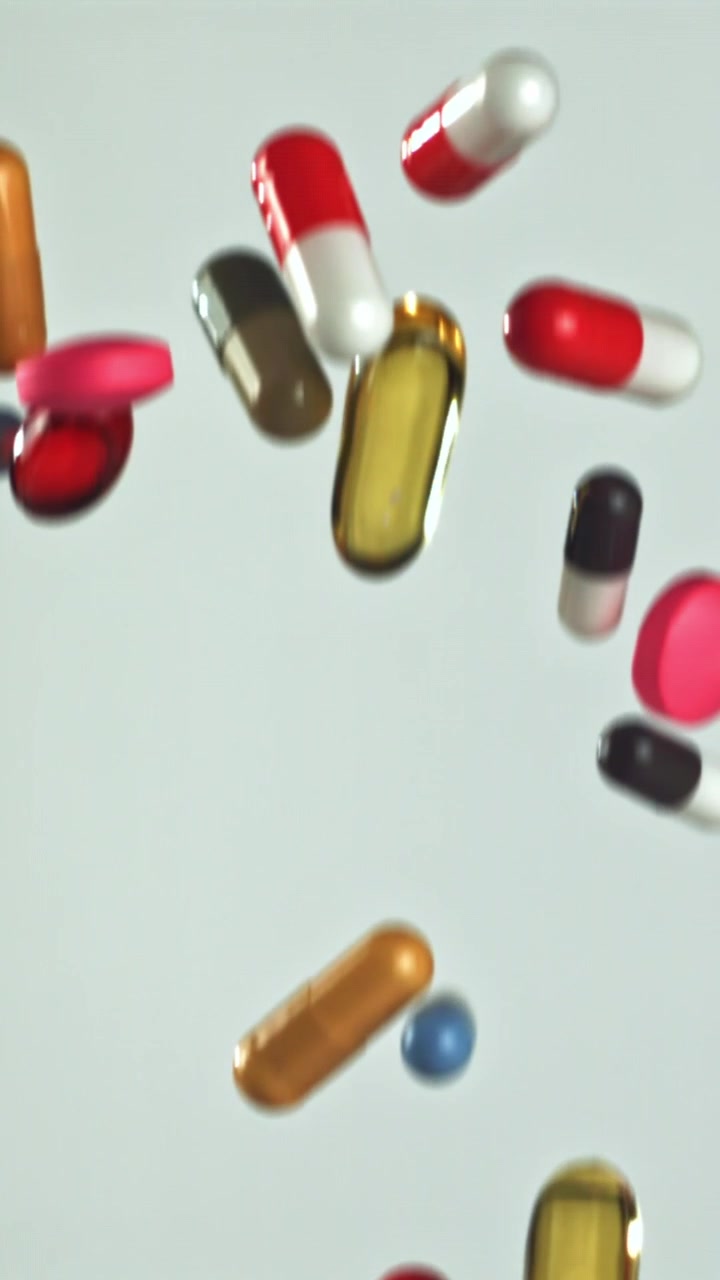 Pastillas y cápsulas de colores cayendo en cámara lenta sobre un fondo blanco