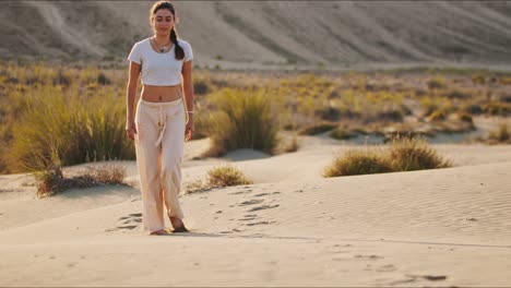 joven instructora de yoga morena caminando hacia la cámara en una colina de arena temprano en la mañana