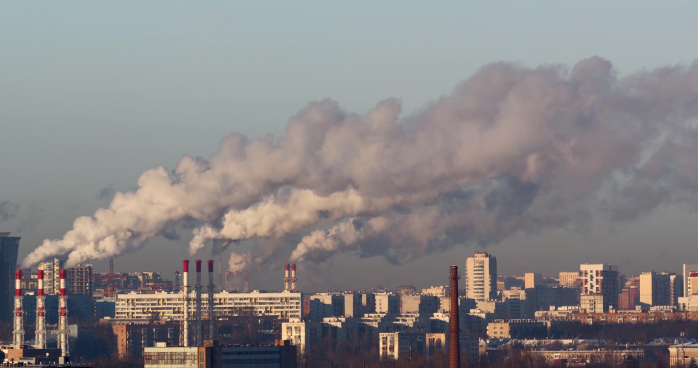 Multiple power plant chimneys release broad layered plumes above a sprawling daylight city with factories offices and apartment blocks illustrating urban energy production and air pollution
