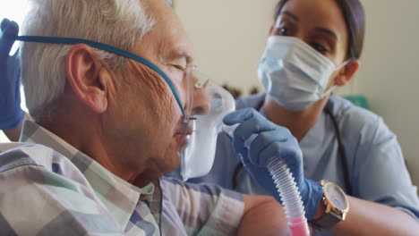 video de una doctora biracial con máscara facial manteniendo oxígeno a un anciano caucásico