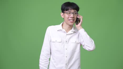 행복 한 젊은 아시아 사업가 가 전화 를 하면서 미소 짓고 있다