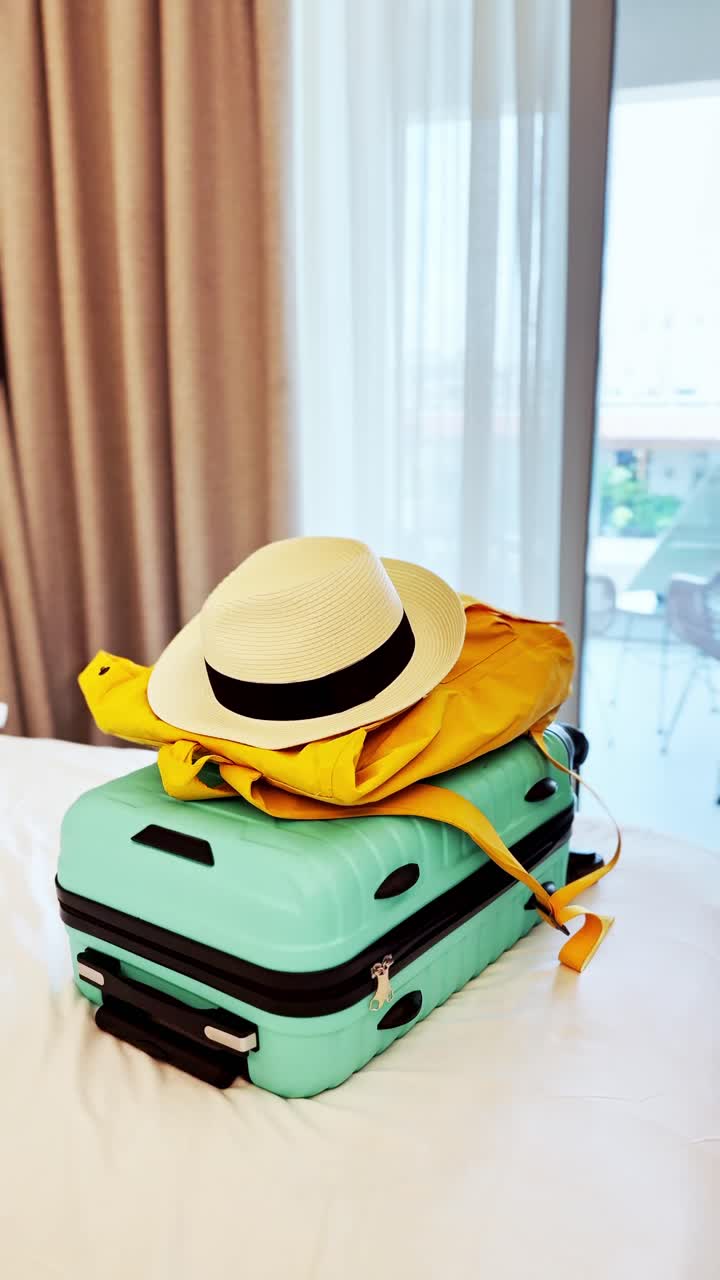 ホテルベッドに置かれた、夏休み旅行の準備ができたスーツケースと黄色のバックパック
