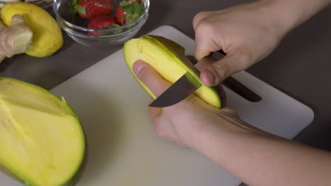 peeling a ripe mango using a sharp knife in the kitchen. - close up shot