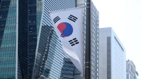 South-Korean-flag-waving-on-the-street-during-day-time-with-skyscrapers-and-sky-on-the-background