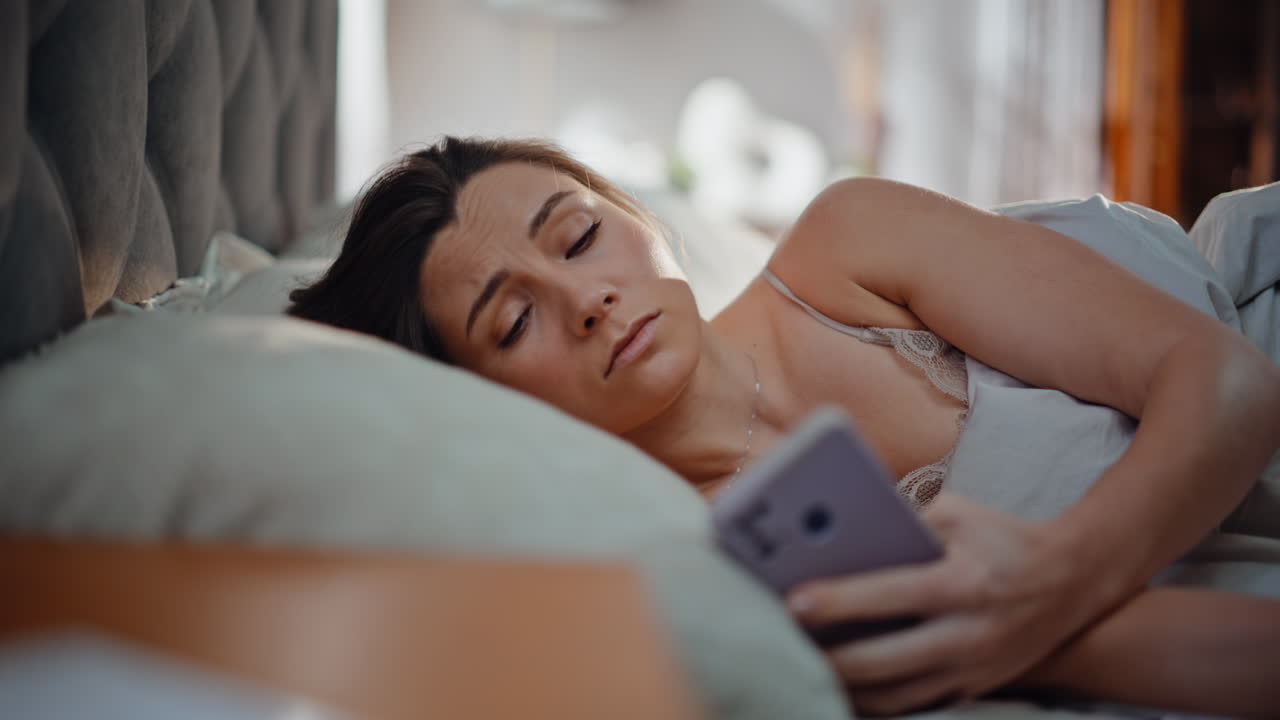 Waking girl taking smartphone lying in cozy home bed closeup. Sleepy woman