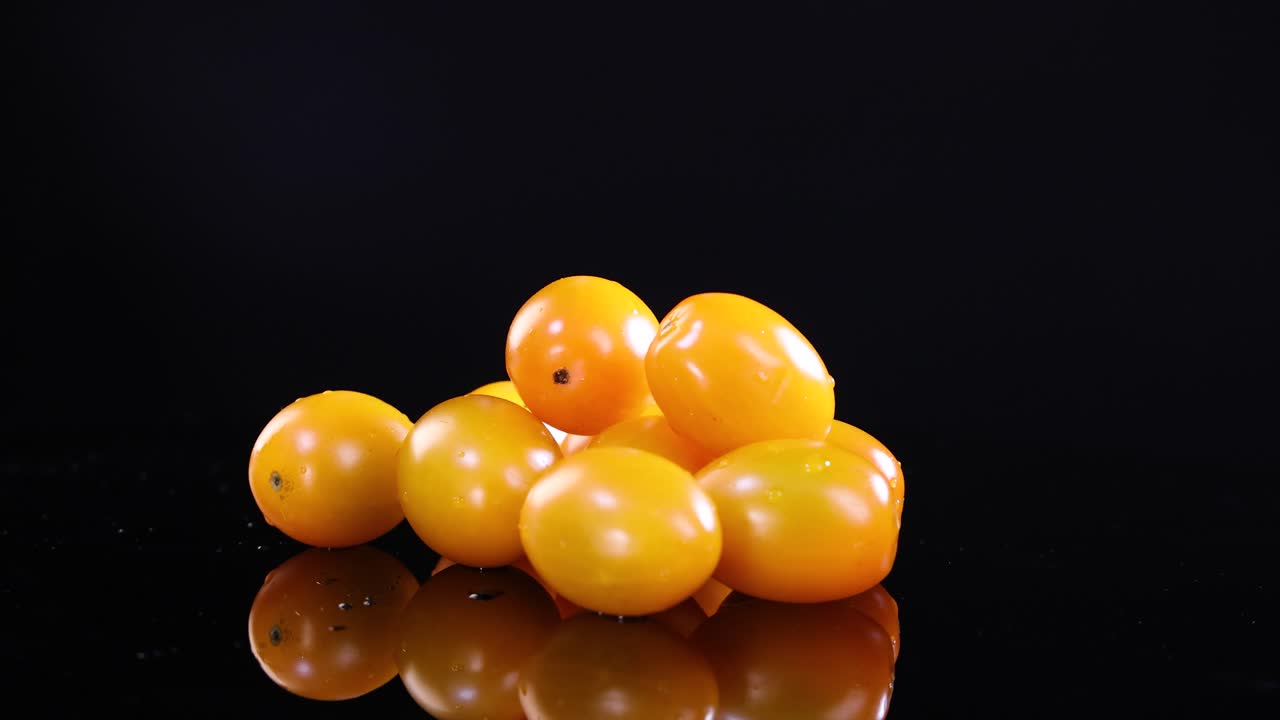 Yellow tomatoes rotate on a reflective black surface under bright lighting, showcasing their glossy texture and vibrant color