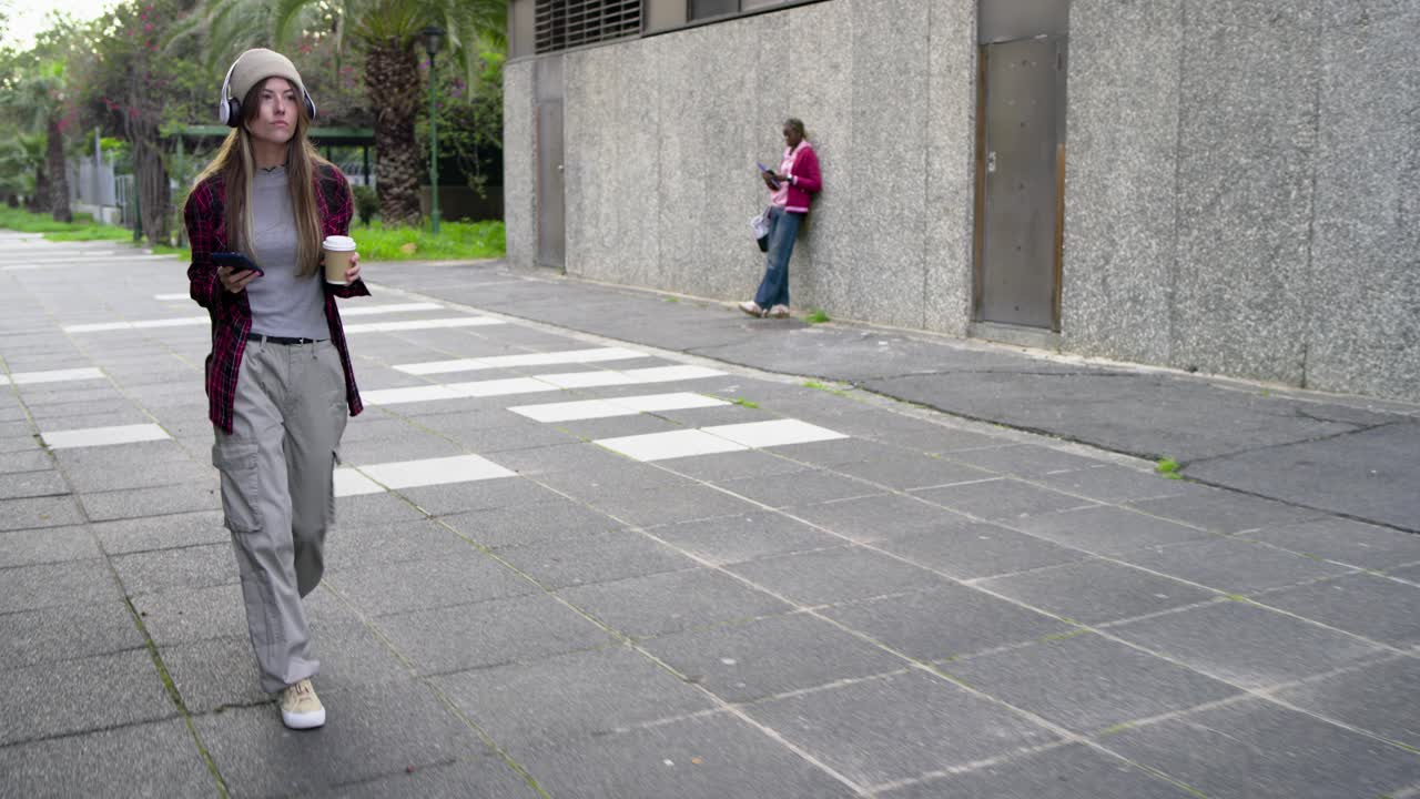 Piétonnes diverses : une femme blanche arrivant par la gauche, marchant, sirotant un café et faisant défiler son téléphone
