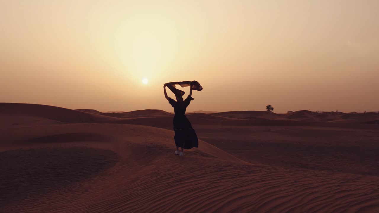 mujer musulmana de pie cerca de la mezquita en el desierto. viento fuerte oriente medio paz sin guerra