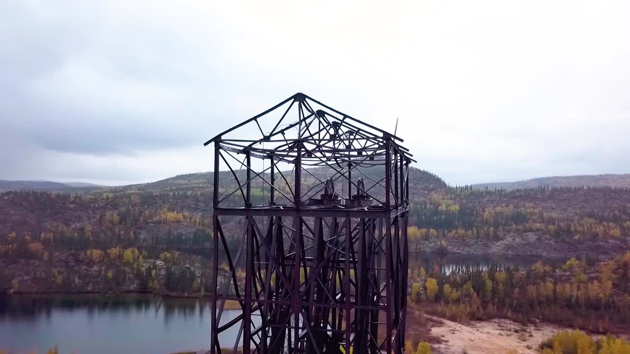 toma panorámica en órbita aérea en cámara lenta de un marco de cabeza de mina abandonada en el bosque boreal en otoño